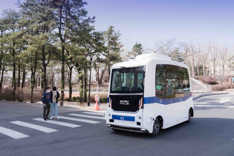 Self-driving Easy Mile shuttle bus approaching pedestrians at crosswalk in wooded area